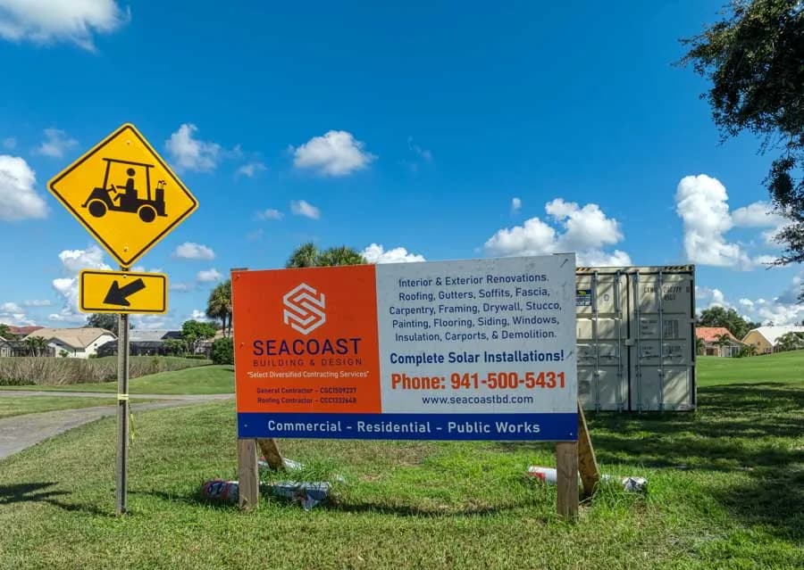 Seacoast Building & Design jobsite sign on a Southwest Florida golf course listing roofing, gutters, solar, and renovation services with the company license numbers