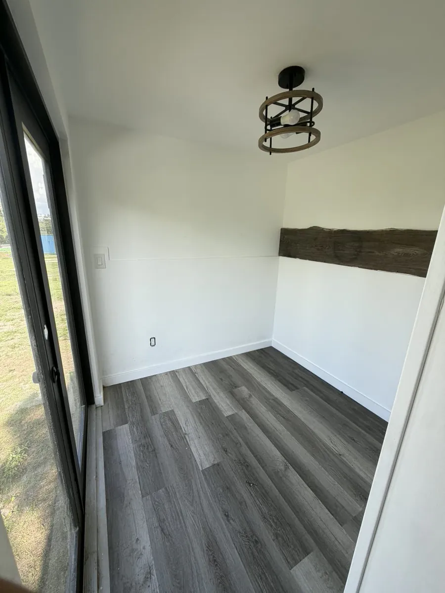 Flex room inside the 20-foot mobile container with wood-look flooring, reclaimed-wood accent trim, and a black-framed glass door