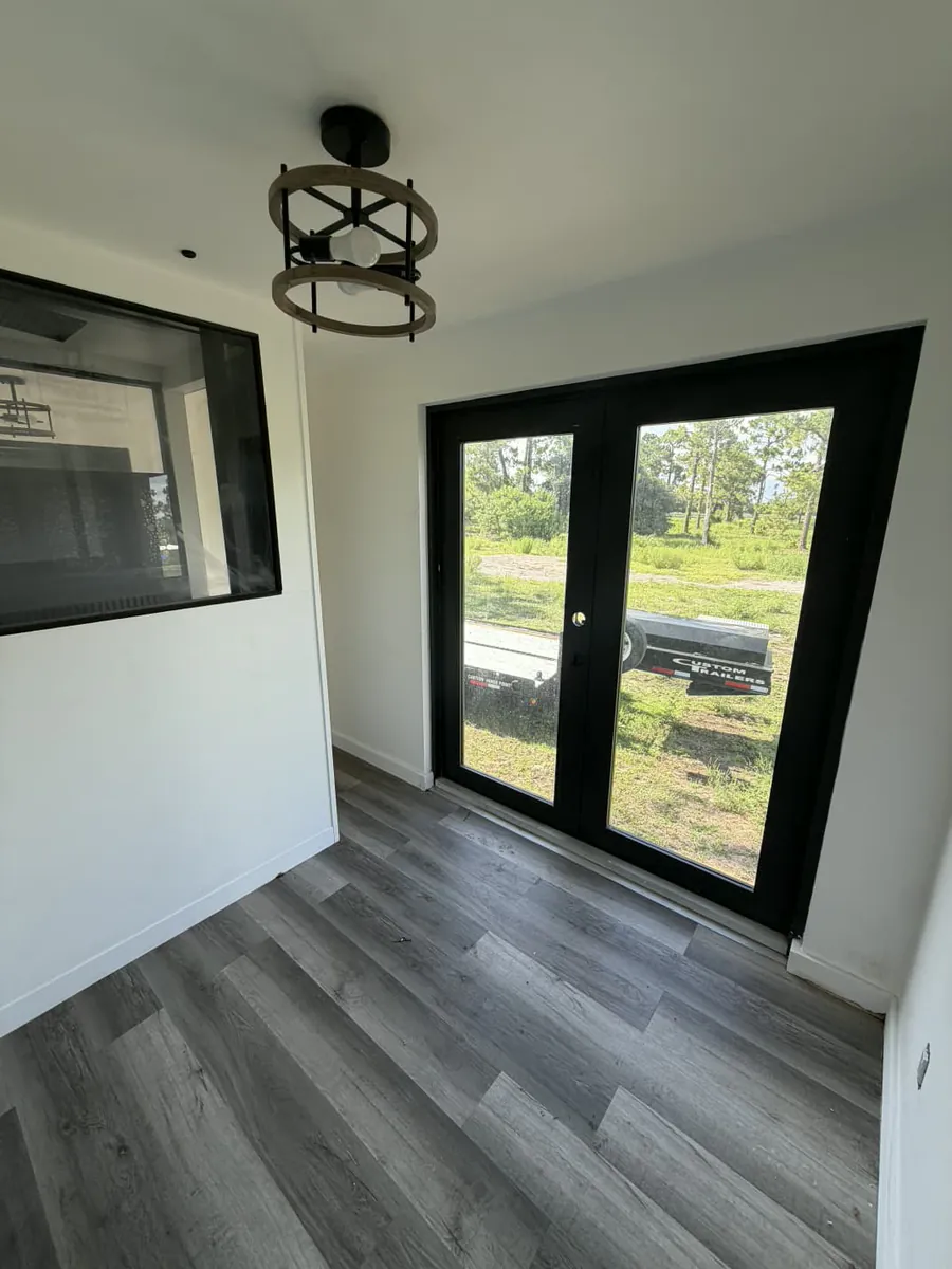 Bright finished room inside the 20-foot mobile container with wood-look flooring, an interior pass-through window, and glass double doors