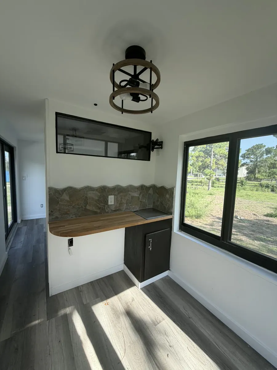 Interior of the 20-foot mobile container showing a butcher-block kitchenette, stone backsplash, cooktop, and black-framed windows