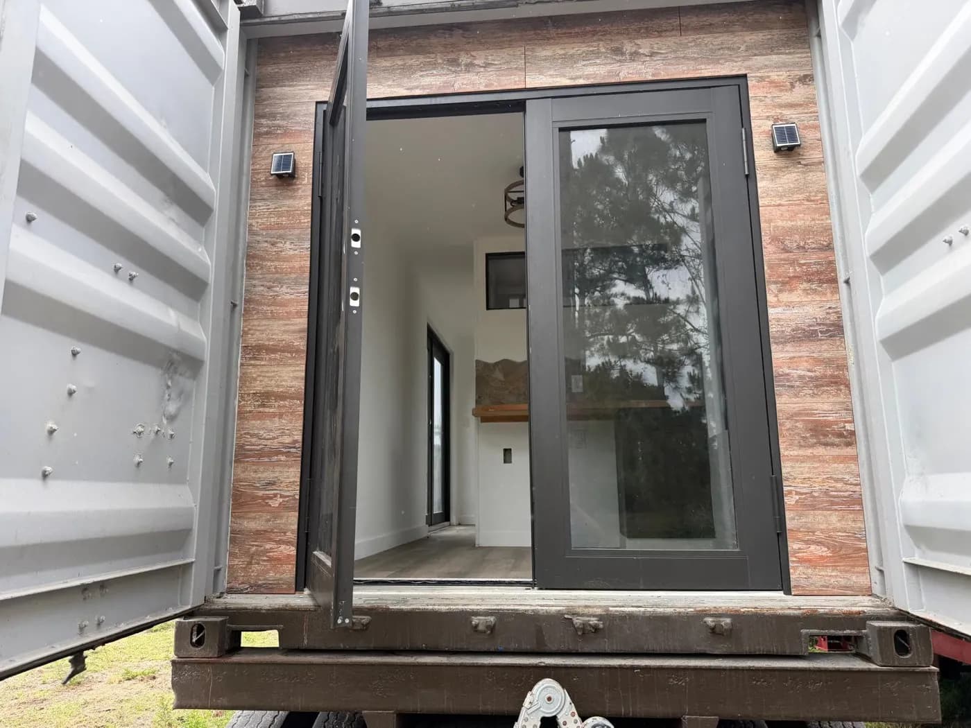 Open shipping-container doors framing glass entry doors and a reclaimed-wood accent wall