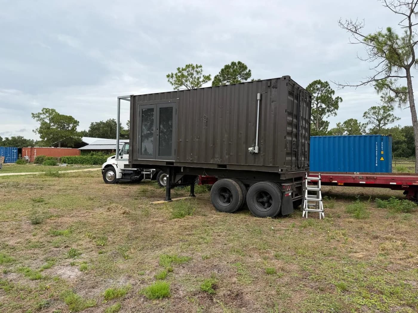 Actual 20-foot container unit shown mounted on its tandem-axle trailer near a transport truck