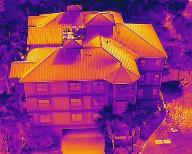 Thermal drone view of the same multi-story Florida building with a metal roof shown in orange and purple surface-temperature colors